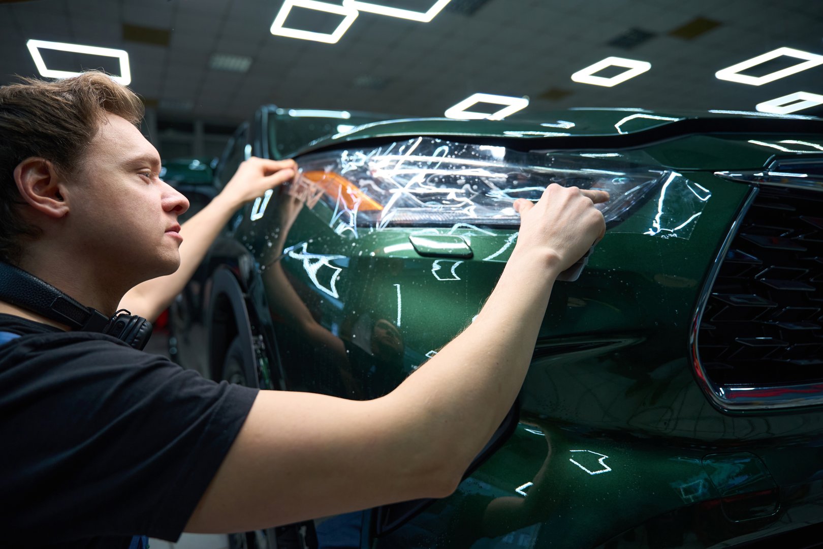 Auto detailing professional adhering protection film to headlight at front of automobile