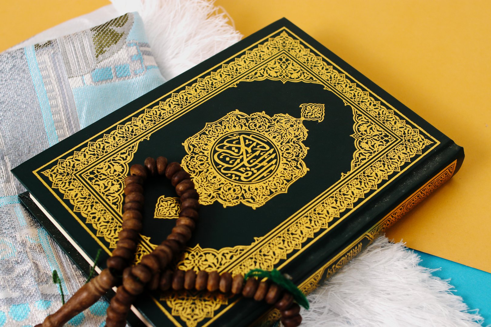 The Holy Quran with a prayer mat and tasbih on a blue and yellow background