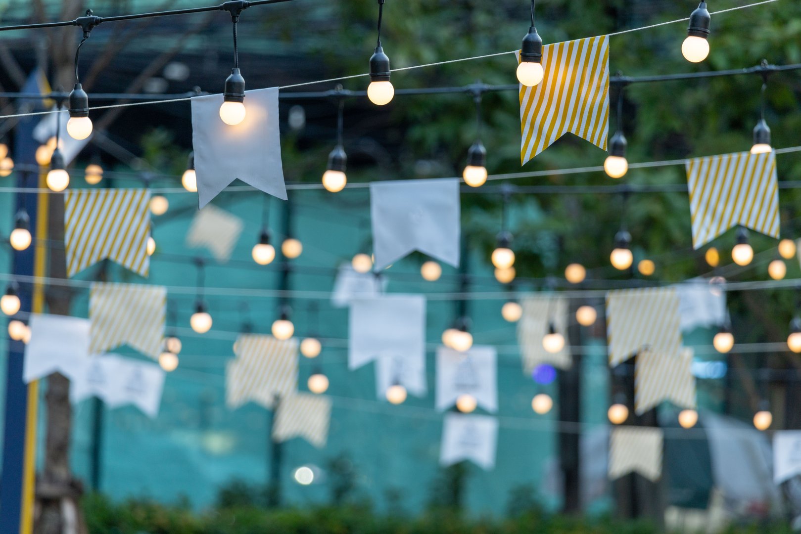 A string of lights with white and yellow flags hanging from them. The lights and flags create a festive and celebratory atmosphere