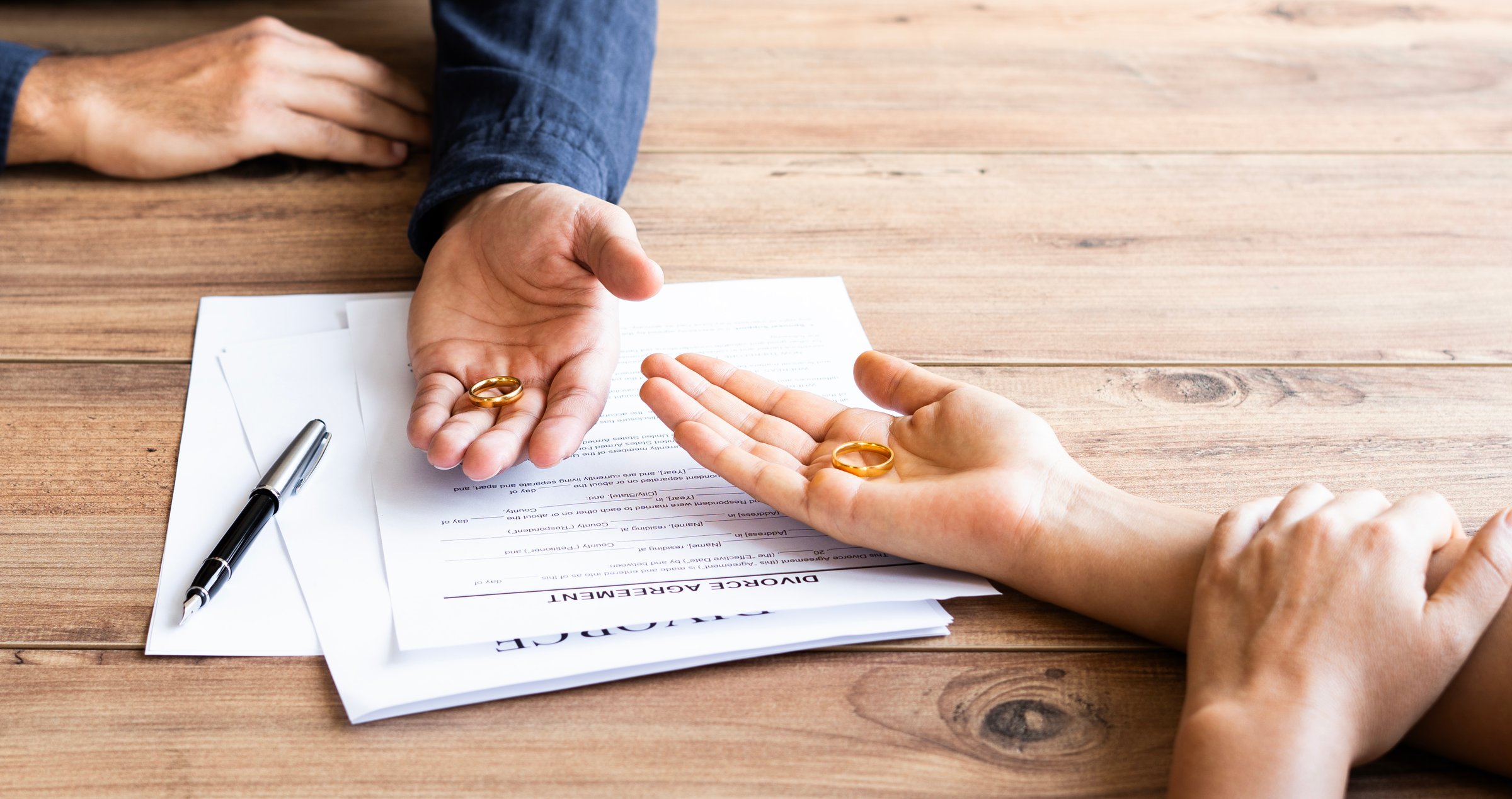 Human hand signing divorce contract, close-up. Wedding rings with marriage contract and judge gavel on a background