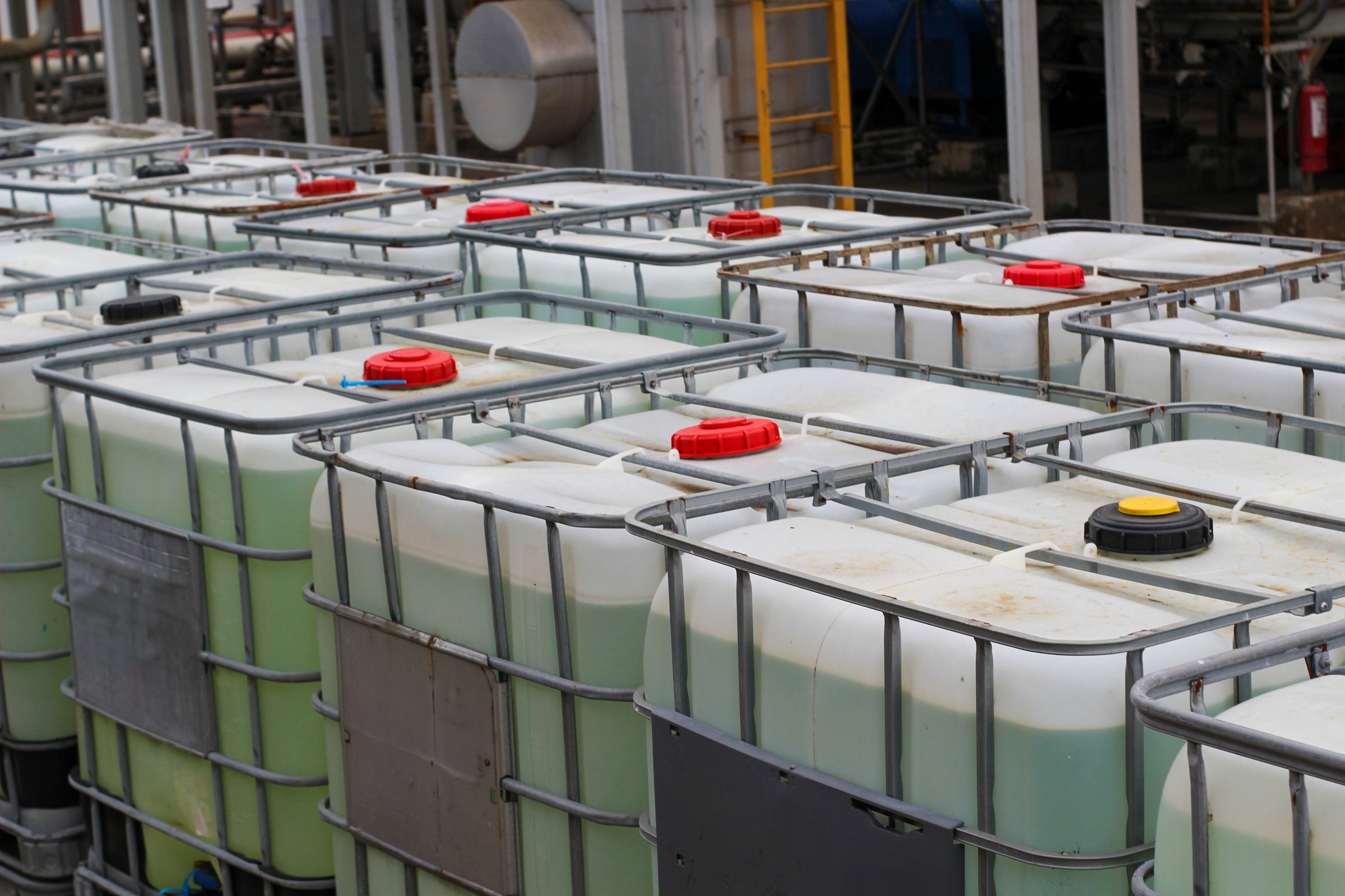 Stacked IBC totes, industrial chemical storage, outdoor setting