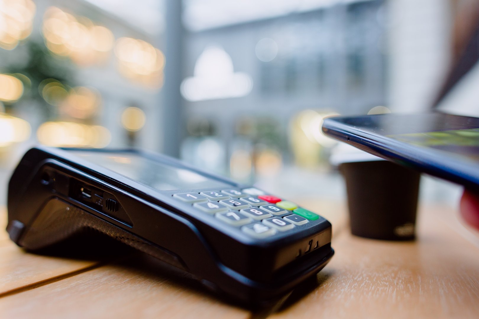 Digital transaction featuring contactless payment method, smartphone tapping payment terminal with blurred retail background, highlighting technological convenience
