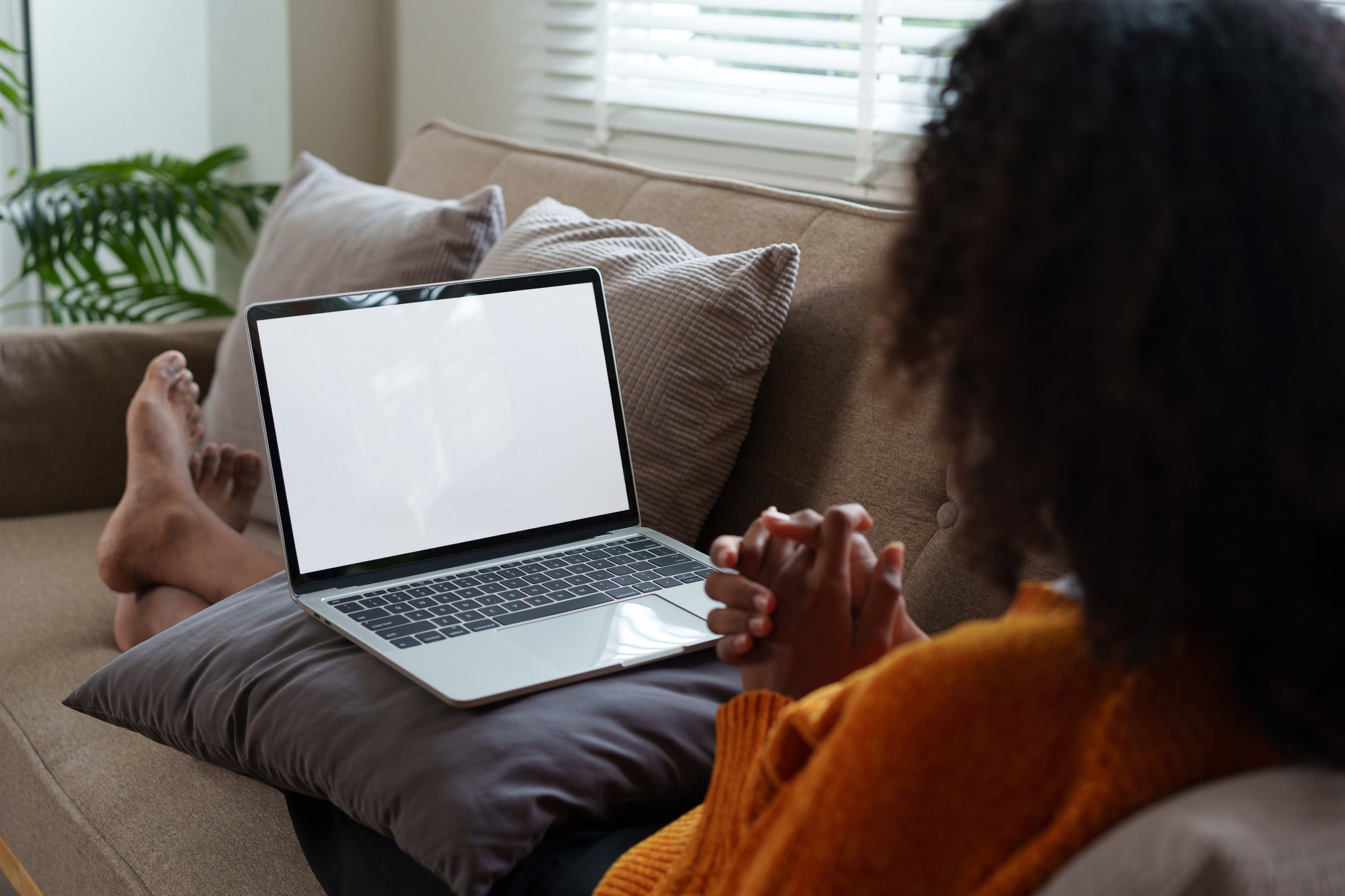 Afro American woman relaxing on couch, using laptop with blank screen at home
