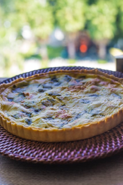 A freshly baked vegetable quiche on a woven placemat, with a blurred outdoor background.