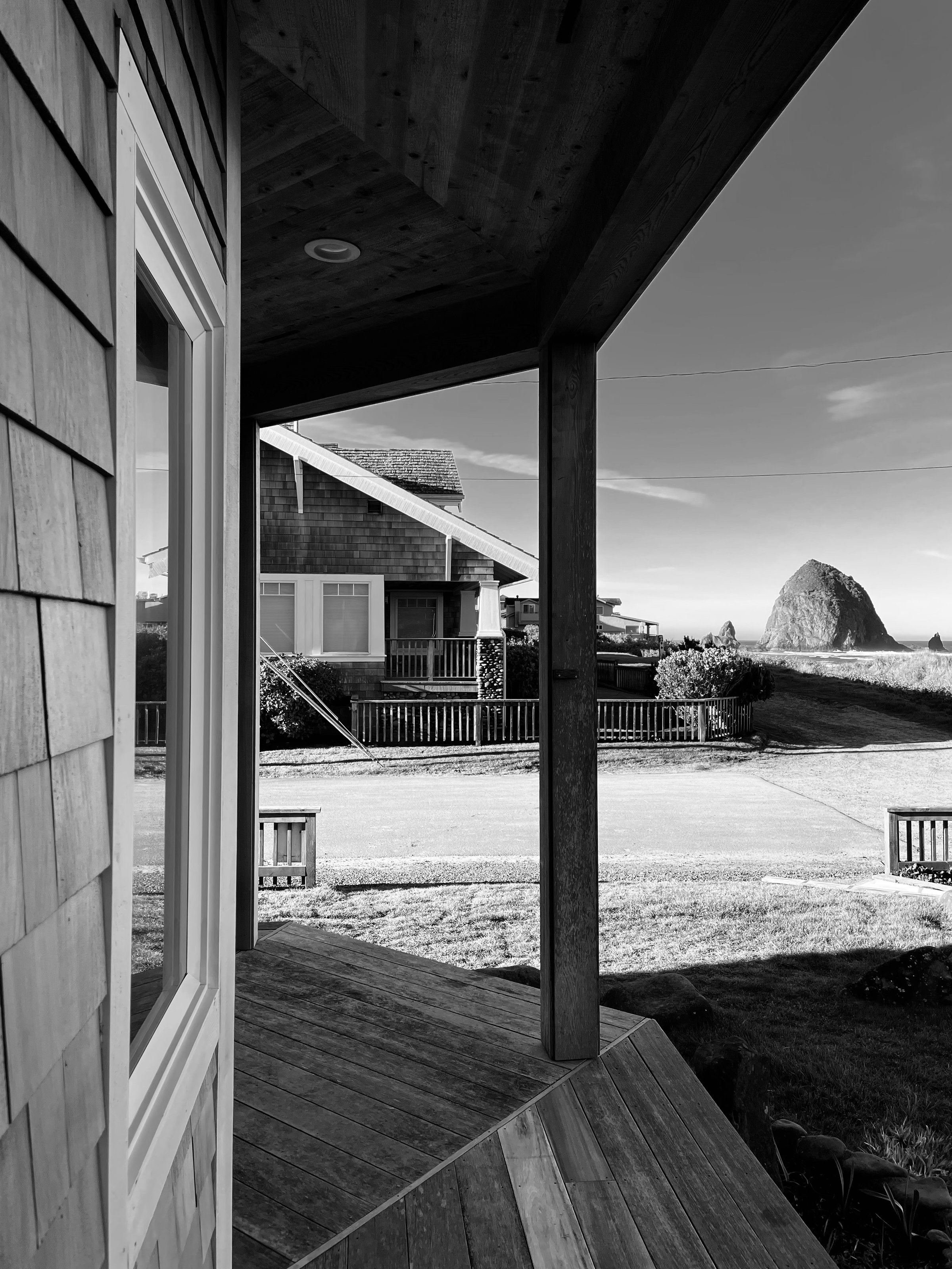 Black-and-white photo of a porch view with a house and rock formation in the background on a clear day.