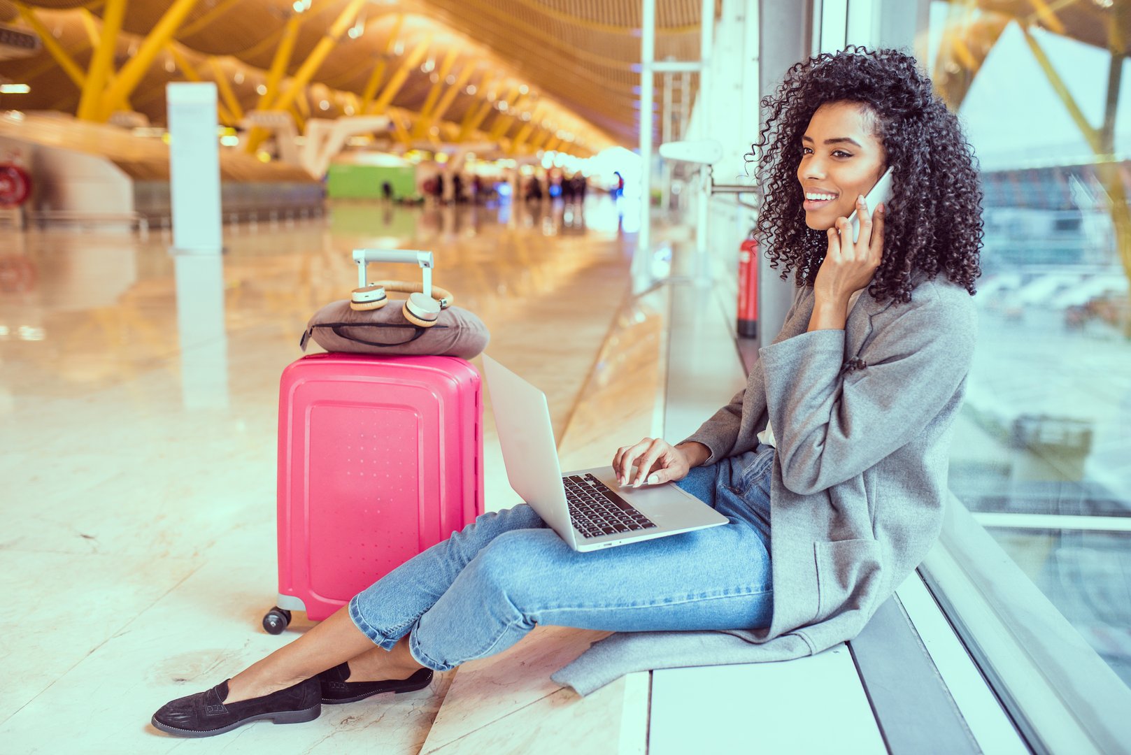 woman using mobile phone and laptop at the airport sitting at the window