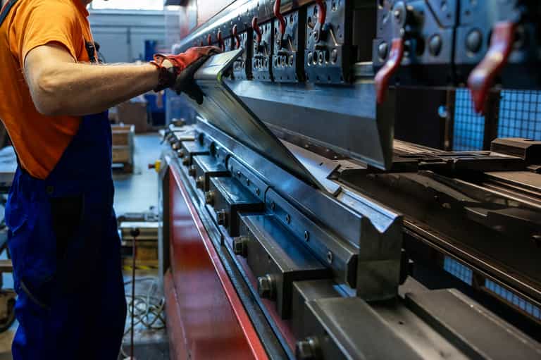 Worker adjusts a large metal sheet on an industrial press, ensuring precision in a busy manufacturing environment.