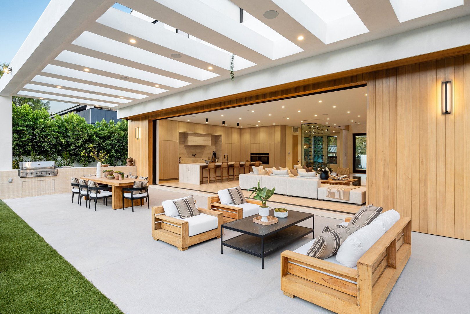 Luxurious modern outdoor patio with wooden furniture and open living space, featuring a seamless indoor-outdoor transition.