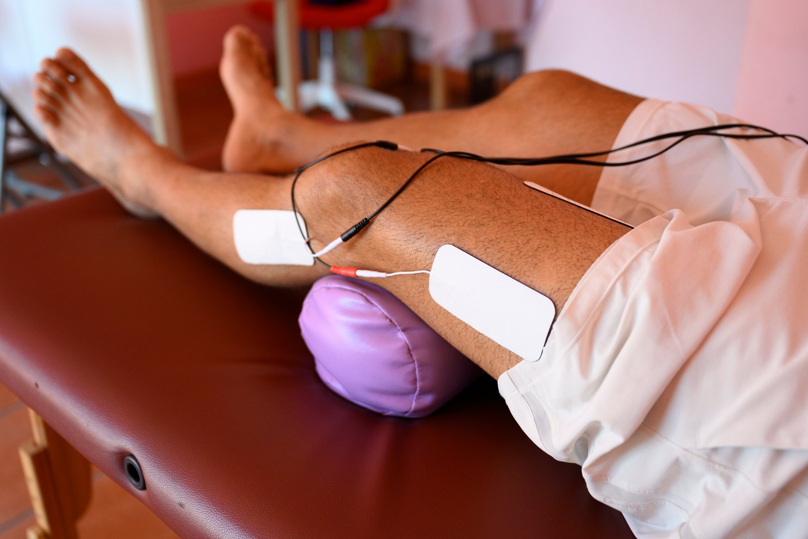 rare view of Patient lies on a physiotherapy table, receiving electrical muscle stimulation therapy on his leg, with electrodes placed strategically to target specific muscle groups