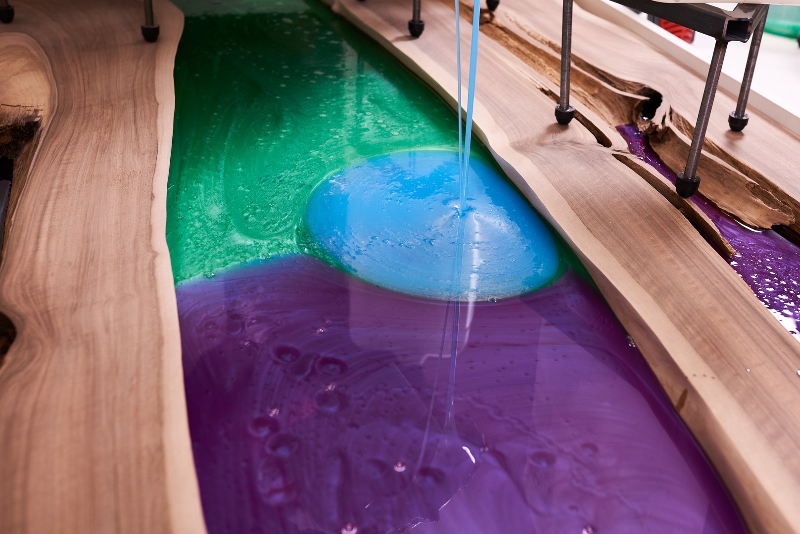 Process making of a craft resin and wood table. Liquid epoxy is poured into a mold with wooden blanks. closeup