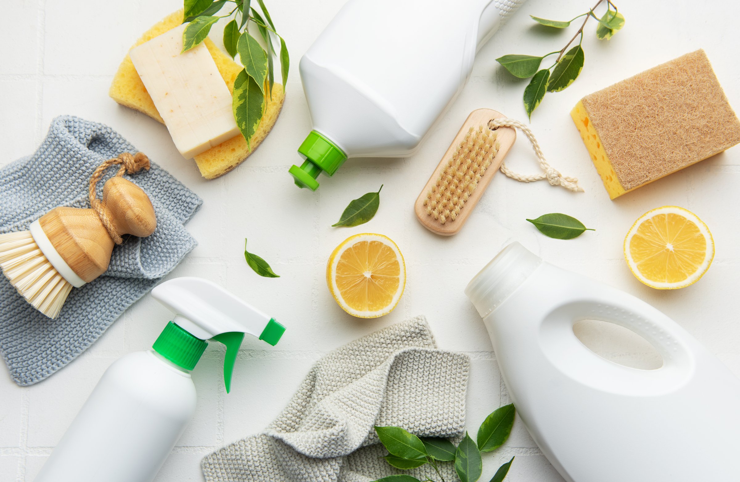 Natural cleaning products, lemon slices, brushes and sponges arranged on white surface promoting eco conscious cleaning routine