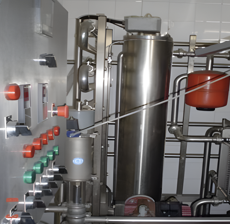 Industrial control panel with buttons and gauges next to metal tanks and pipes in a processing facility.