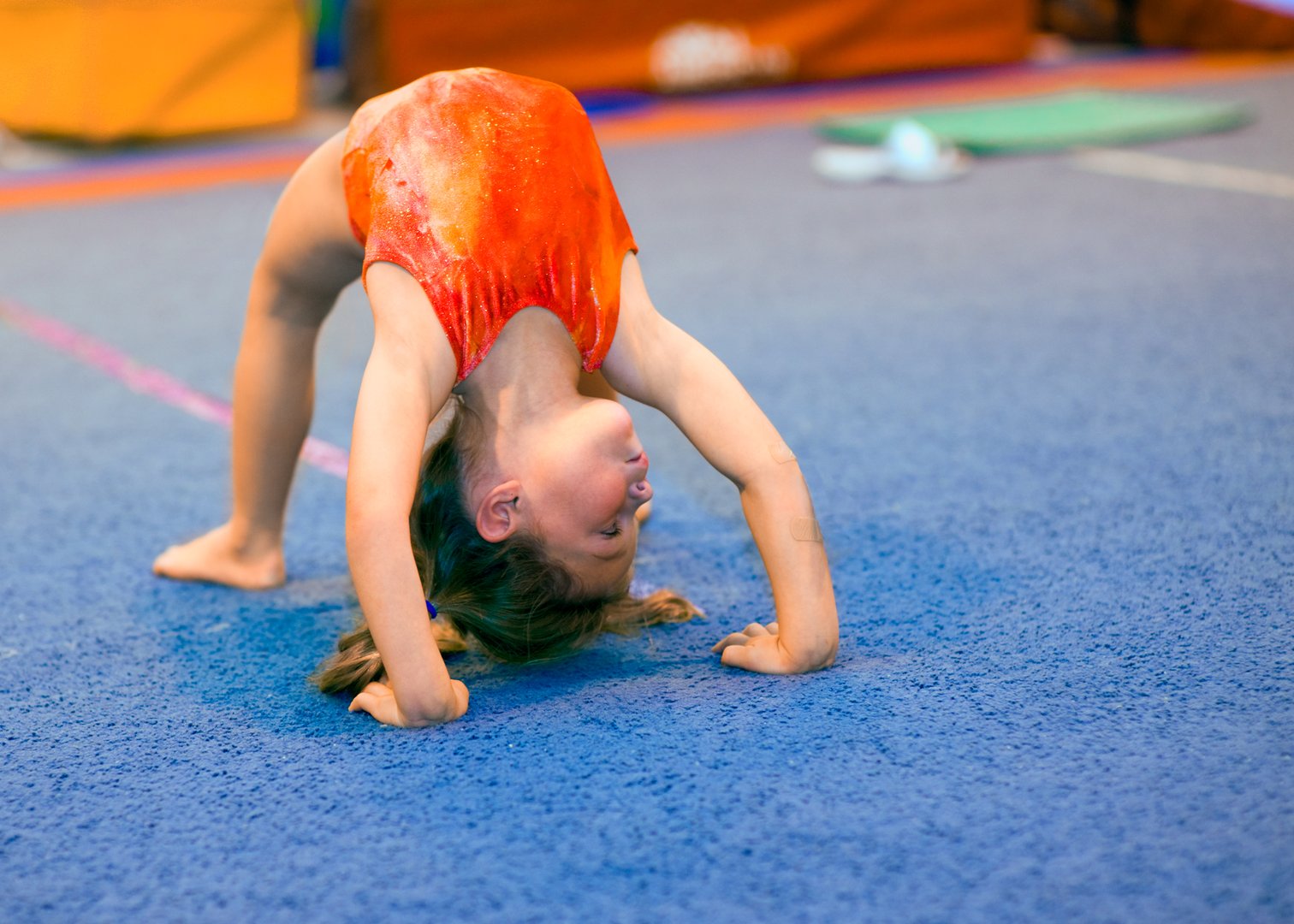 Children can excel at gymnastics, even beginning at a very young age! This toddler girl, aged 4, is demonstrating a Bridge position by pushing off her hands and feet and thrusting her back upwards. She is looking right.