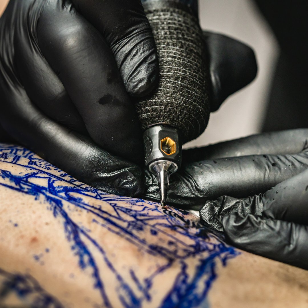 Professional master tattoo artist drawing tattoos picture on man's back using machine wearing black gloves at studio salon body art