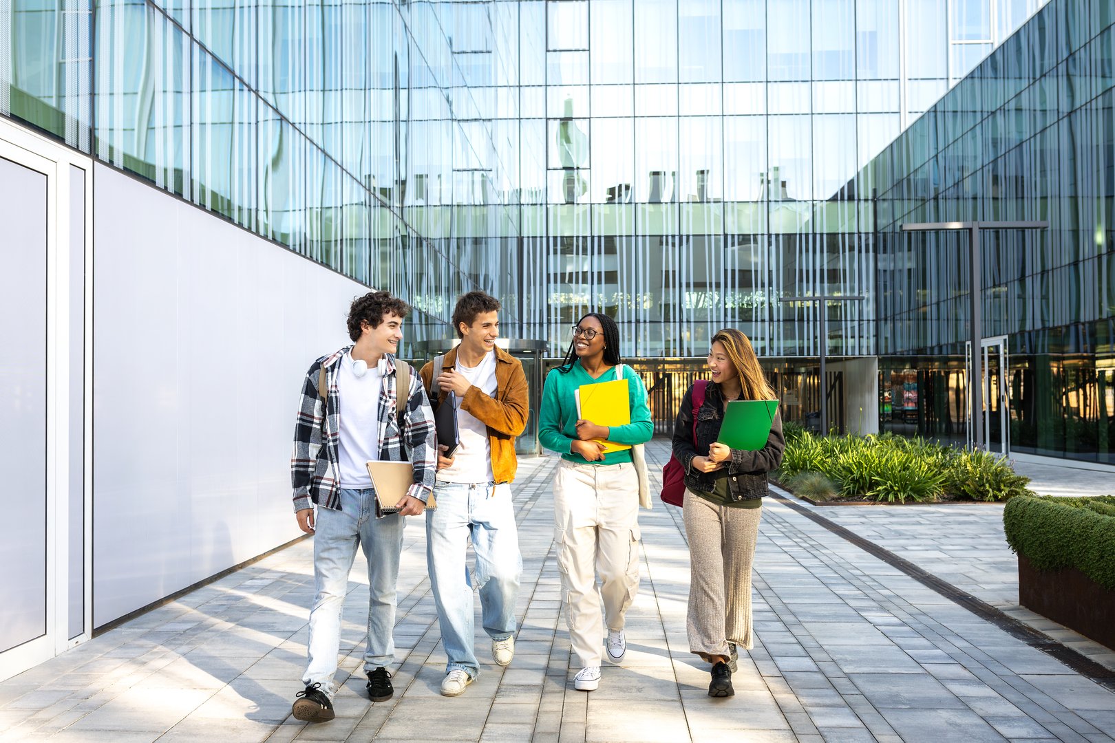 Four cheerful university students walking and talking together outside campus buildings