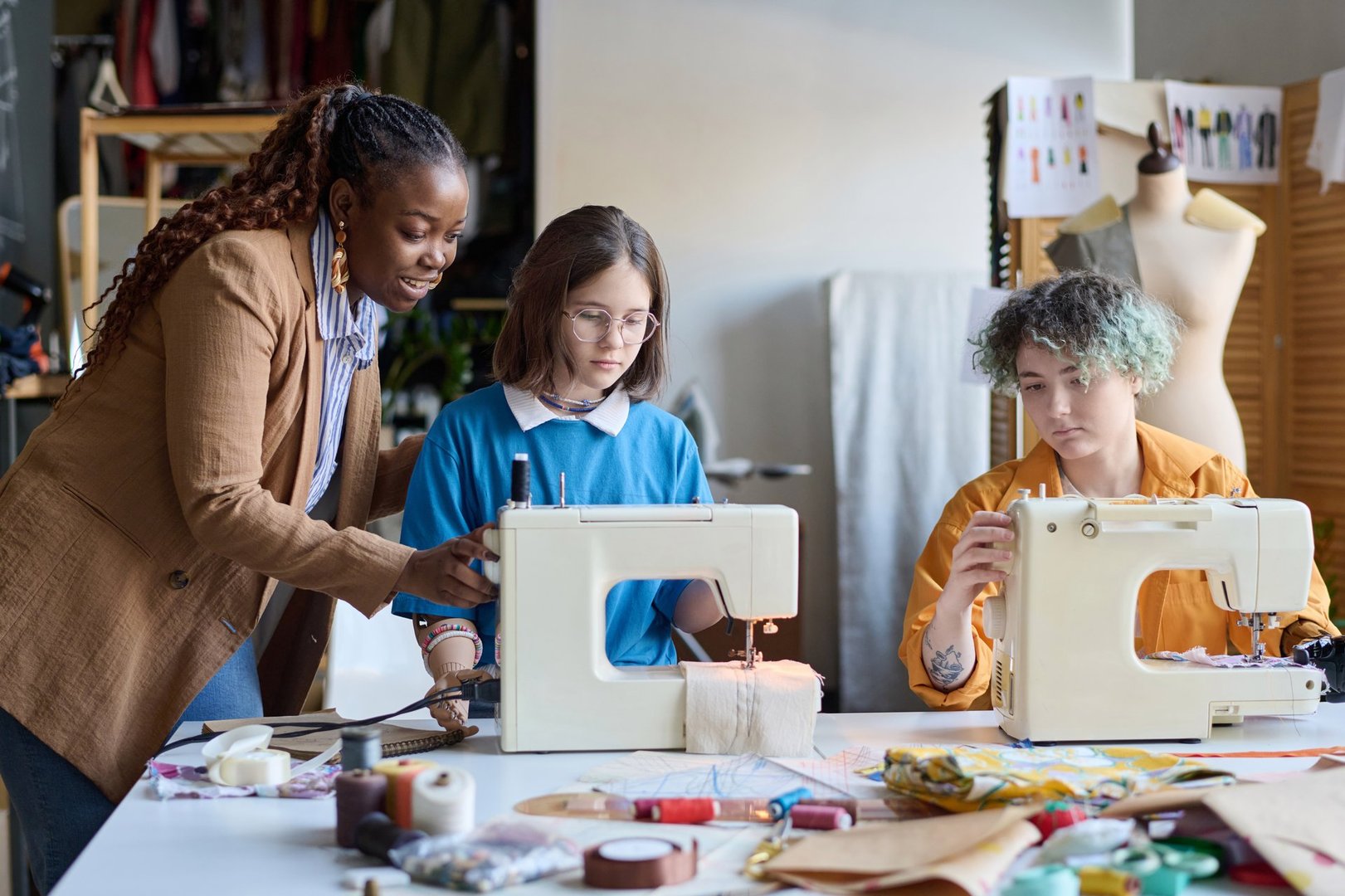 Portrait of African American young woman helping girls with disabilities using sewing machines in vocational training class copy space