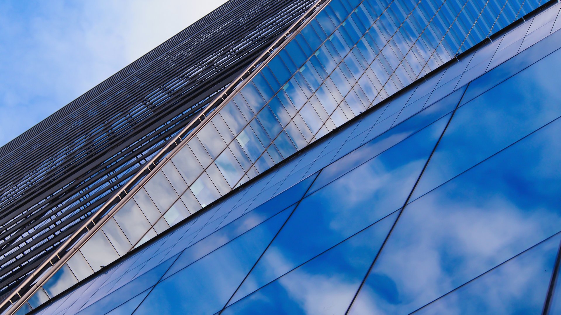 the dynamic interplay of light and reflections on a modern glass building, highlighting clean lines and geometric patterns.