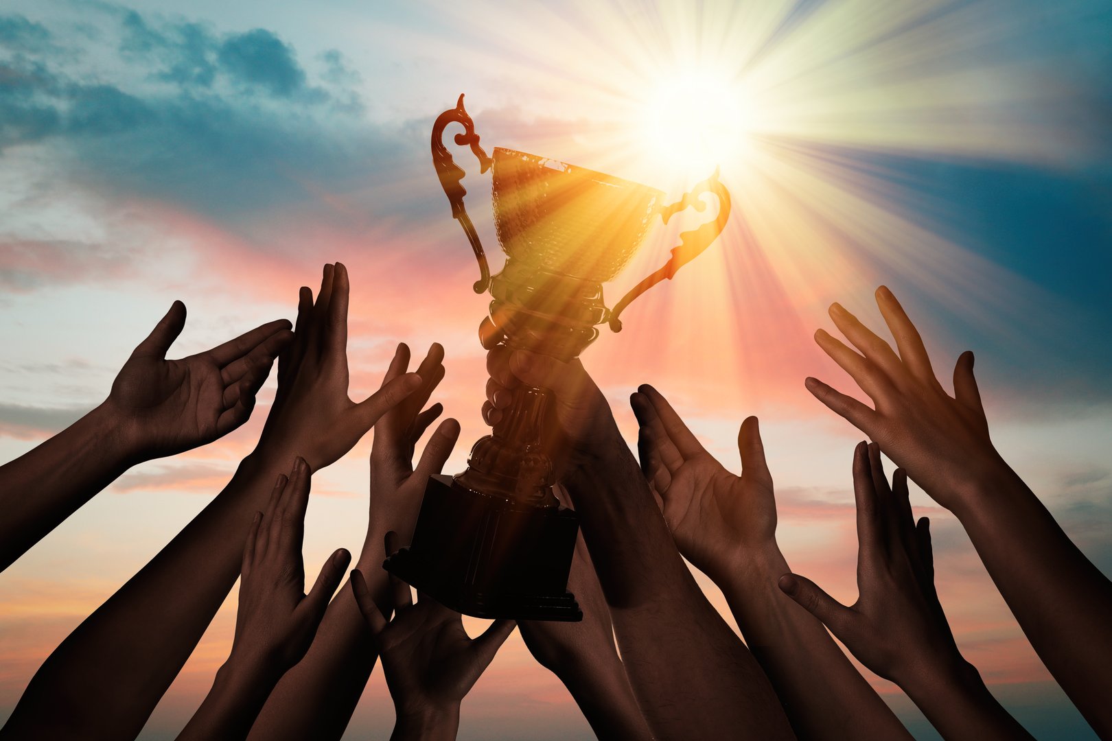 People reaching for a trophy against a sunset. For motivational business campaigns, team achievement awards, and corporate success celebrations. Inspires aspiration, recognition, and teamwork.