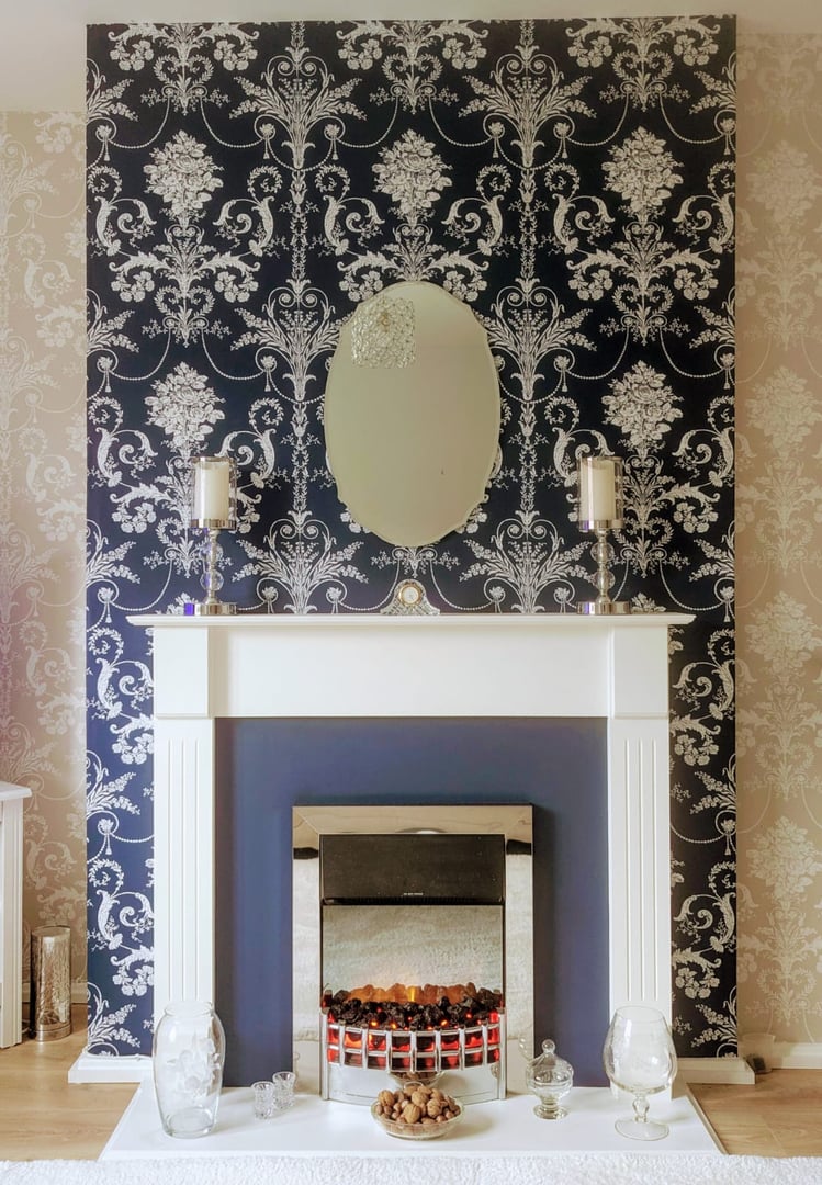 Elegant fireplace with ornate navy and white wallpaper, mirror, candles, and decorative items on the mantle.