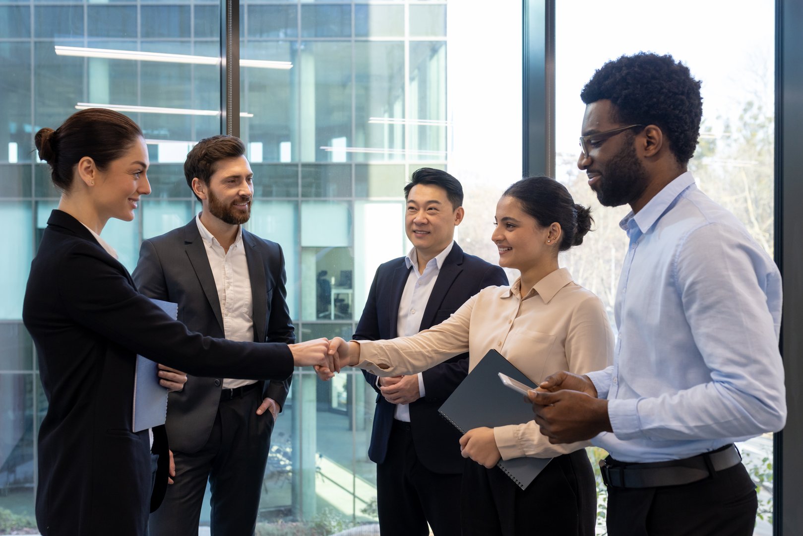 A diverse group of business people shake hands in an office setting, symbolizing agreement and teamwork.
