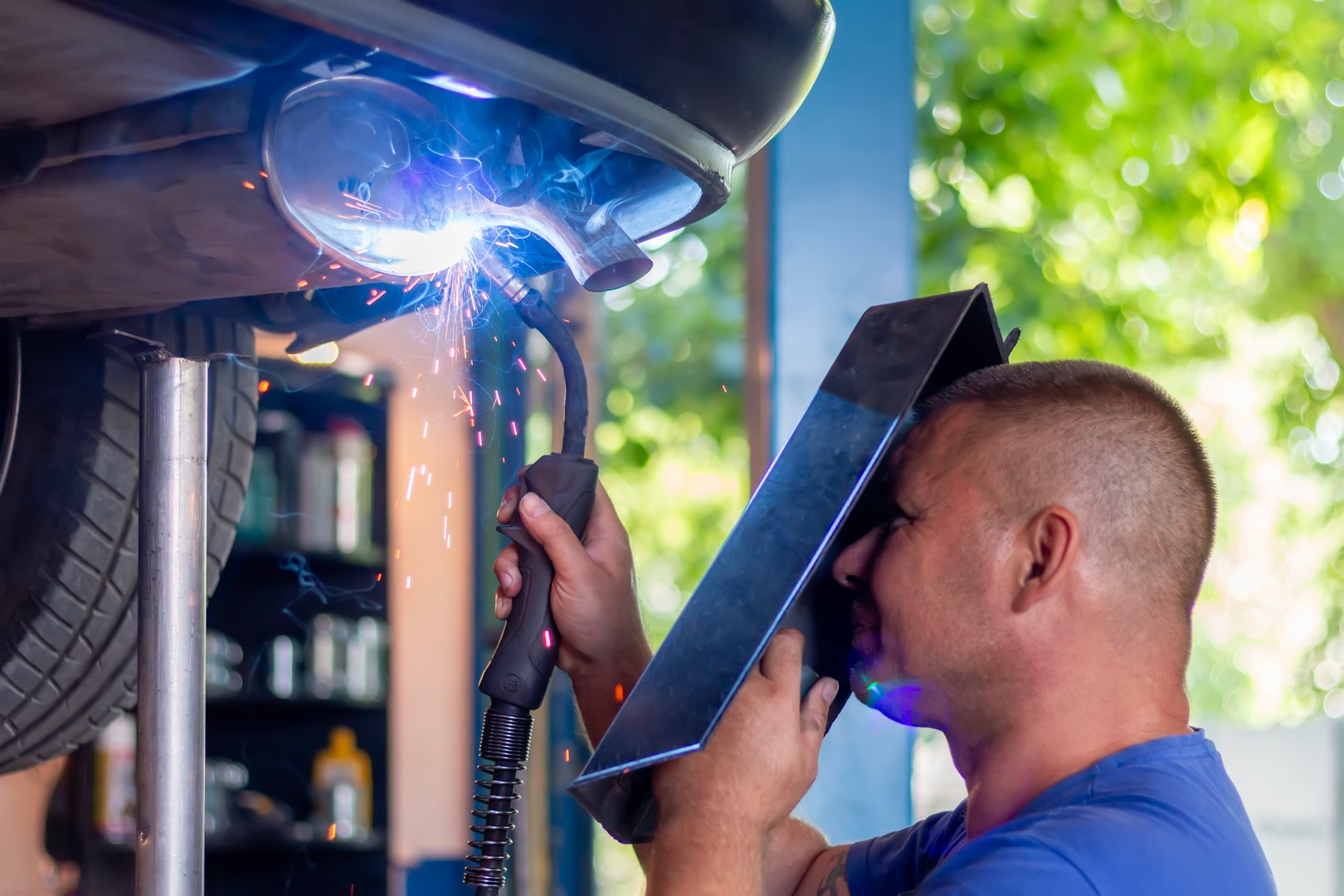Auto mechanic performing essential car repair by welding an exhaust pipe on a vehicle lifted at a professional workshop, ensuring quality vehicle maintenance and service