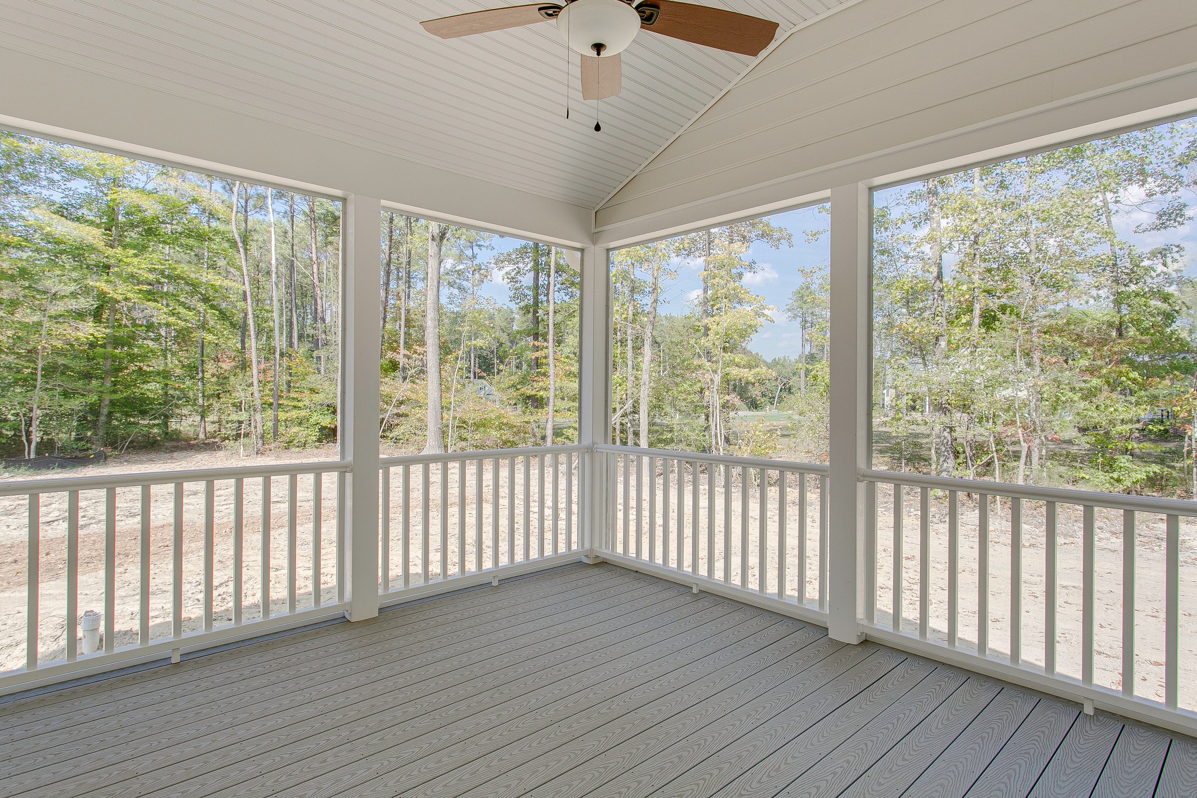 A cozy screened porch featuring a ceiling fan overlooking a serene natural landscape, perfect for relaxation and enjoying the outdoors in comfort.