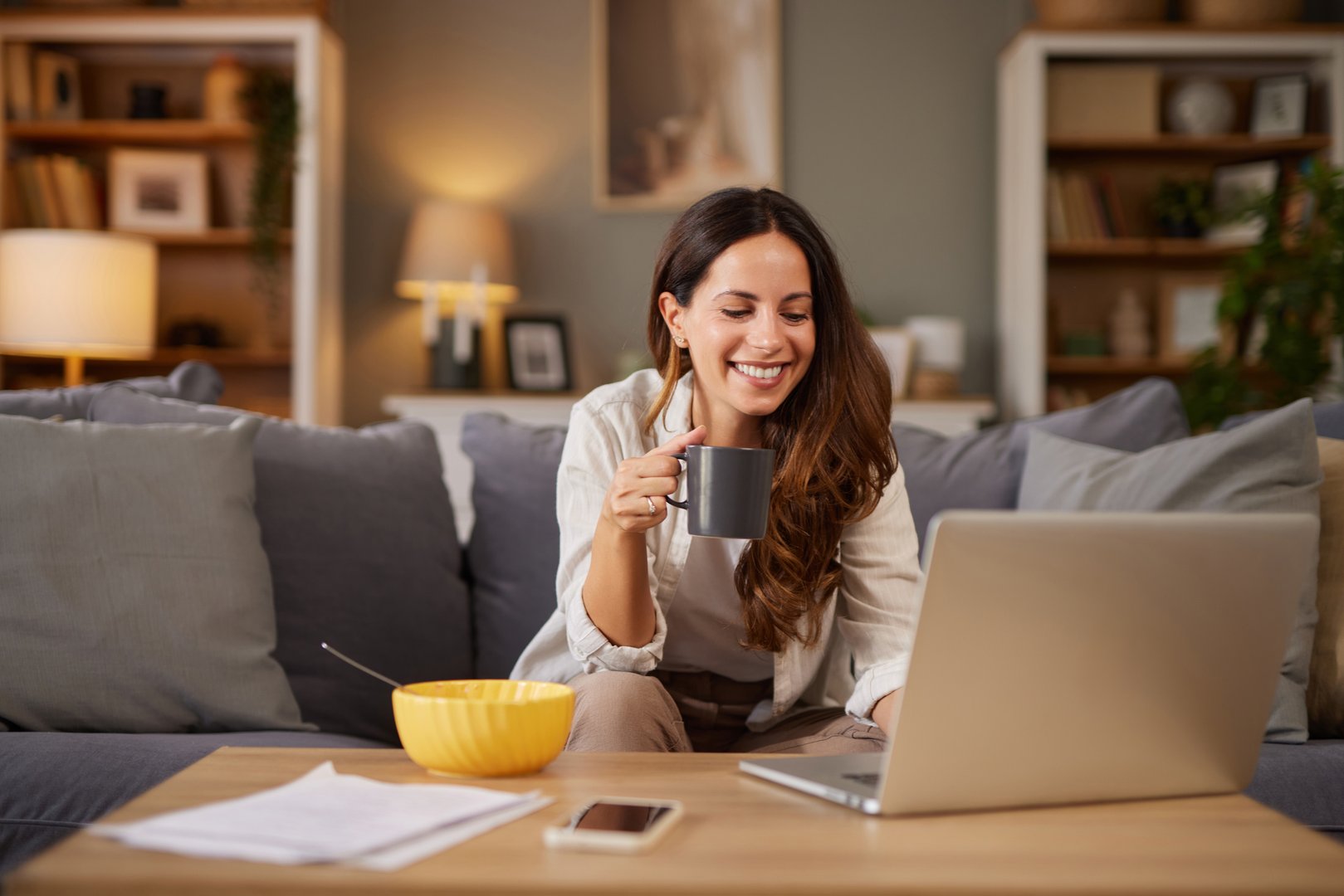 Woman enjoying a coffee and breakfast while using a laptop from her cozy home