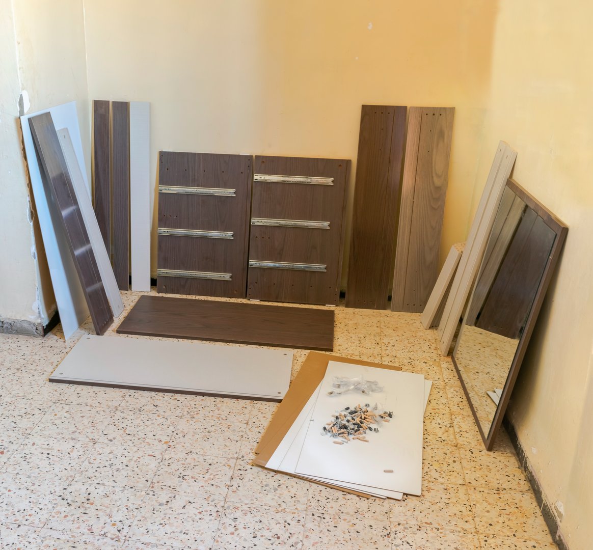 Displayed and placed against the wall, including a mirror and drawers with hardware on the floor, ready for assembly.