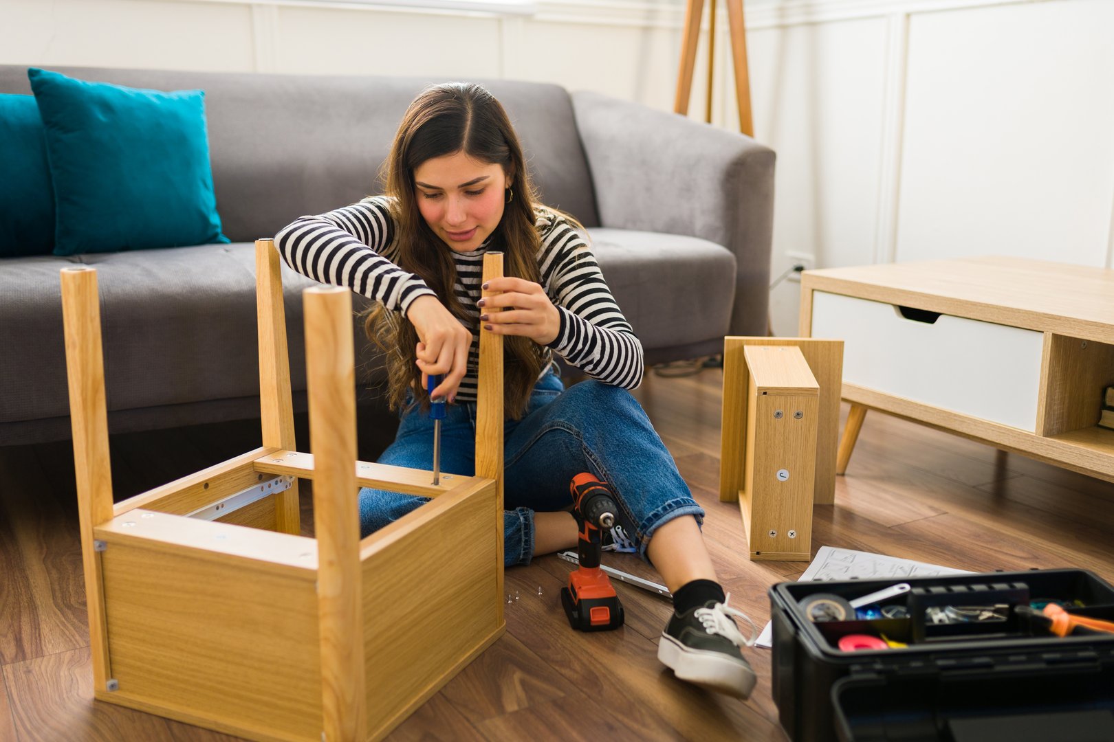 Happy beautiful woman assembling a table with a screwdriver and tools while furnishing her home