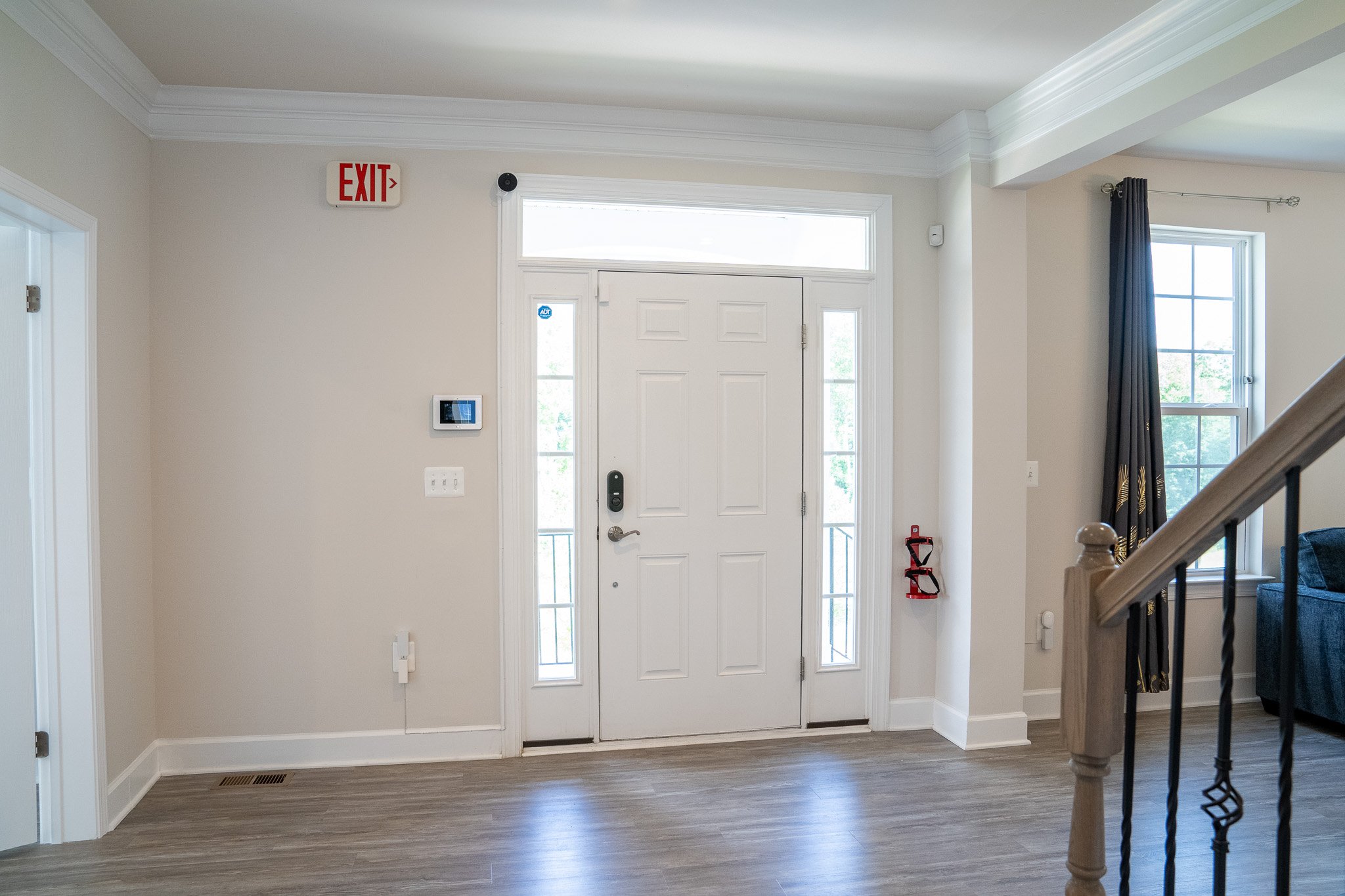 Interior of a modern living space with a front door, exit sign, wall thermostat, and white walls and flooring.