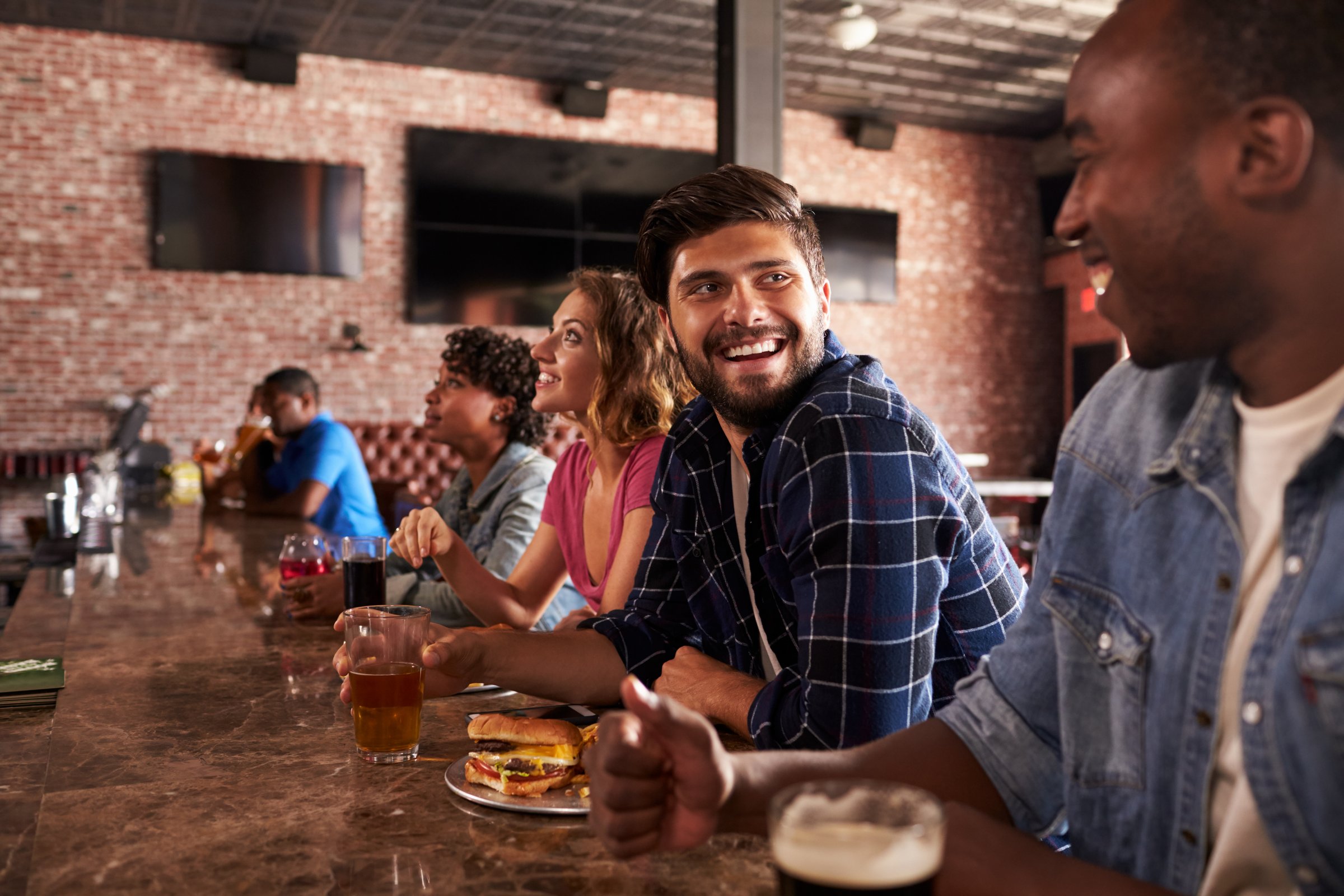 Friends At Counter In Sports Bar Watching Game
