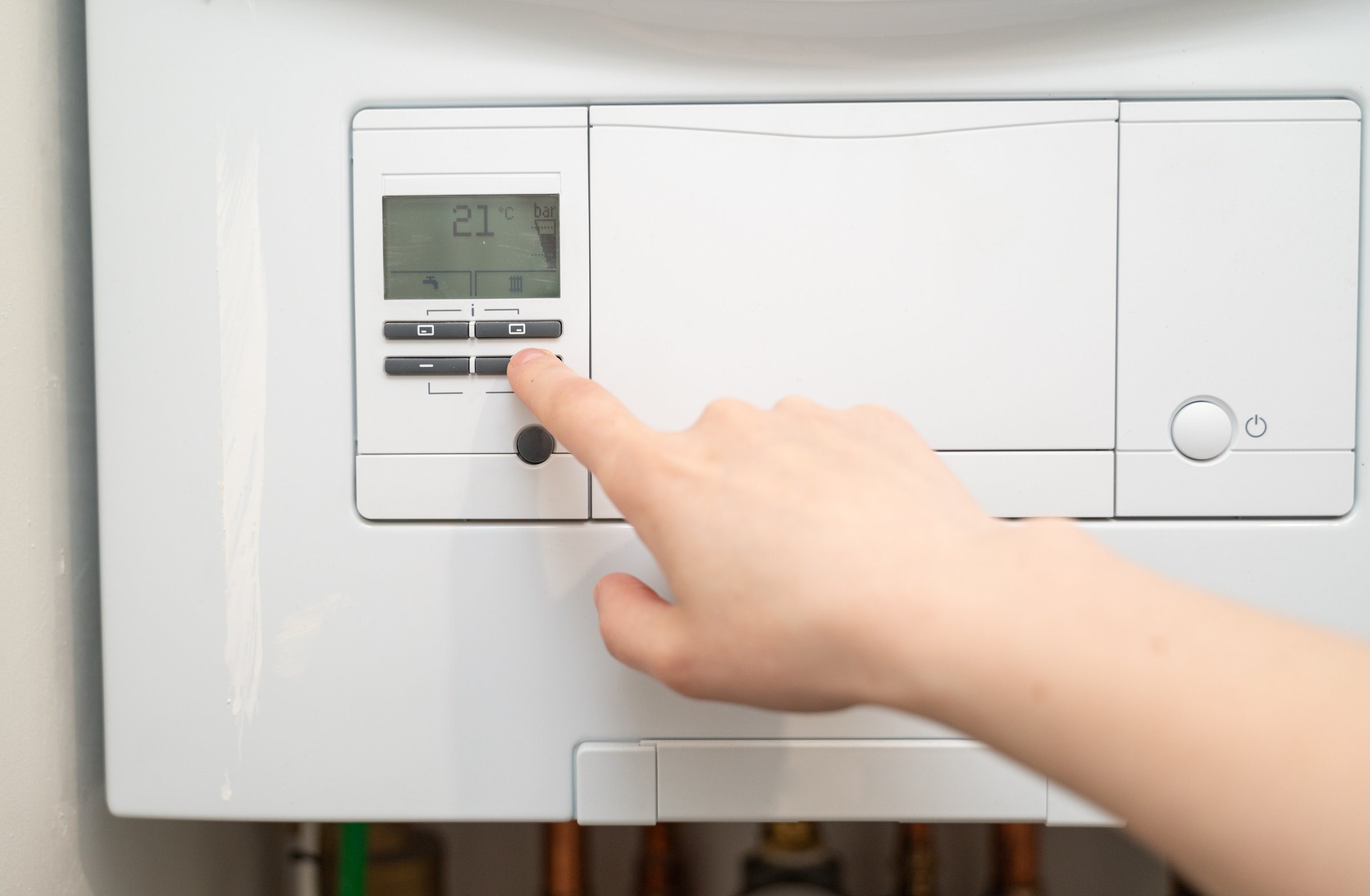 A hand is carefully adjusting a thermostat in a contemporary heating system to achieve the perfect temperature
