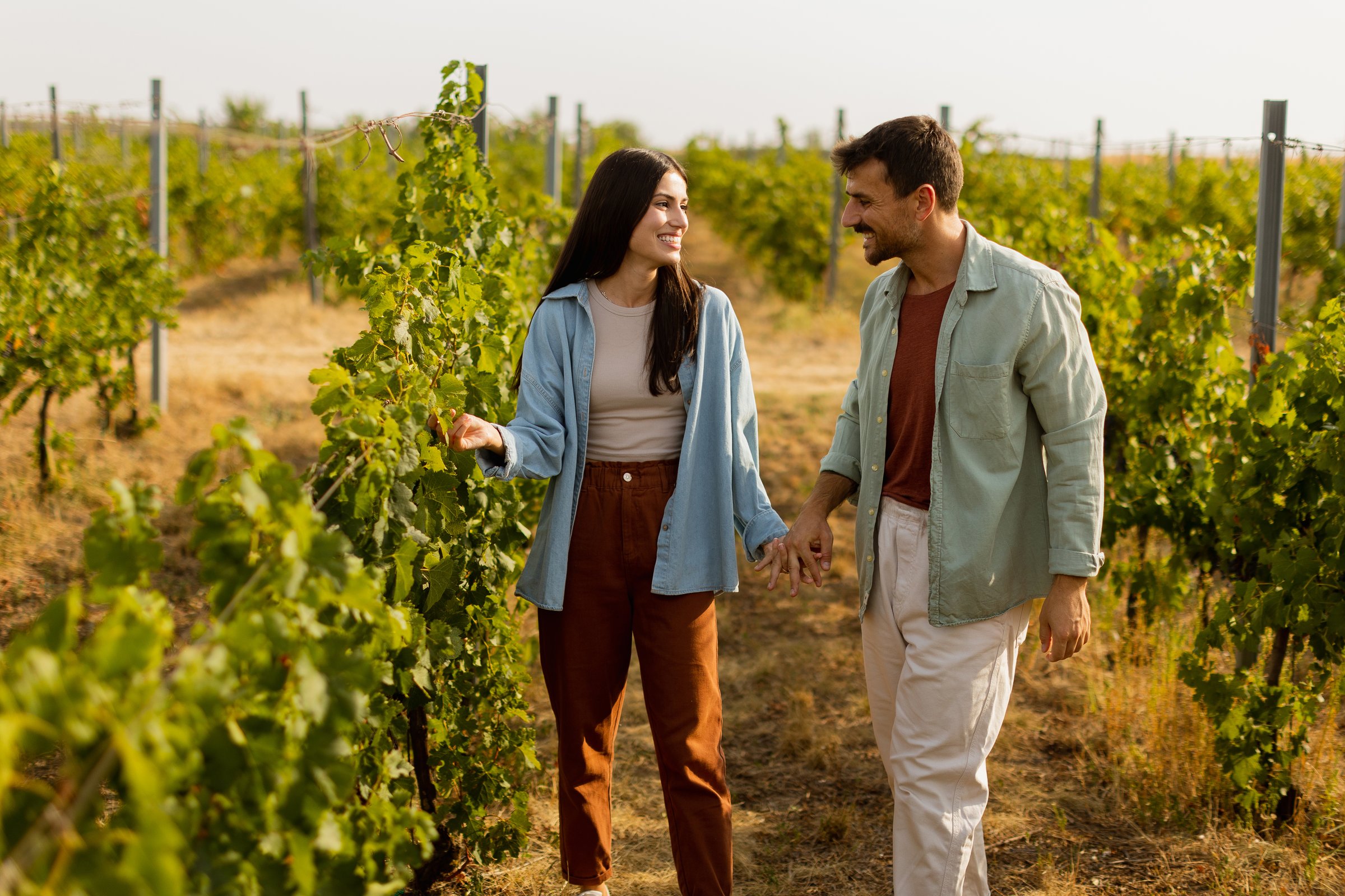 Young couple shares a joyful moment among verdant vines, laughing and embracing under the warm sun, celebrating love and the serenity of a picturesque vineyard