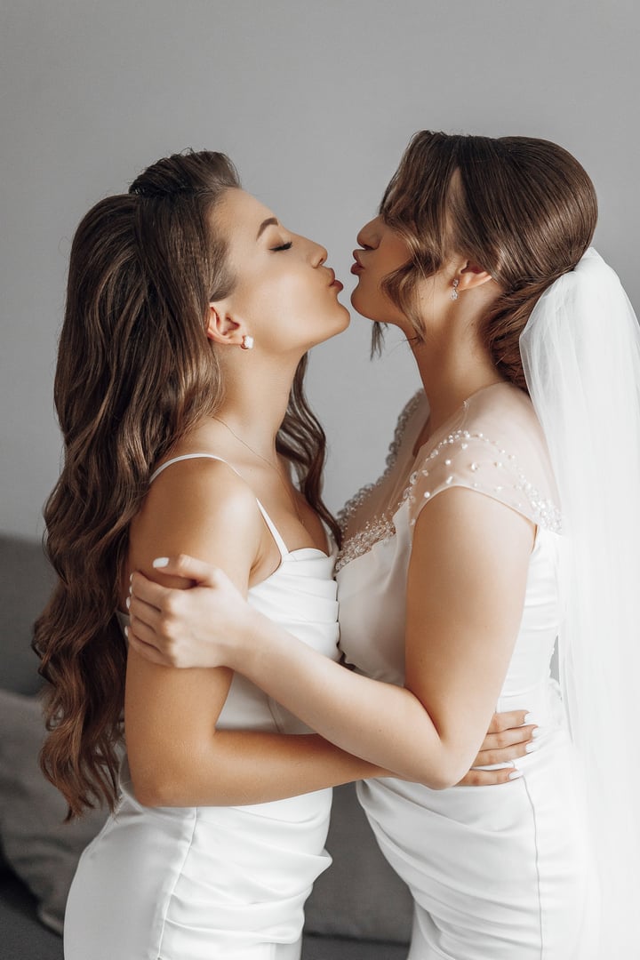 Two women kissing each other, one of them wearing a wedding dress. The image has a romantic and intimate mood