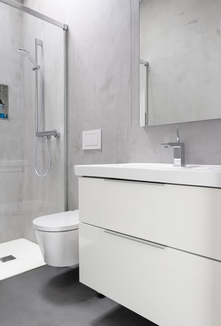 Modern bathroom with grey microcement on walls and floor and white furniture. Minimalist interior