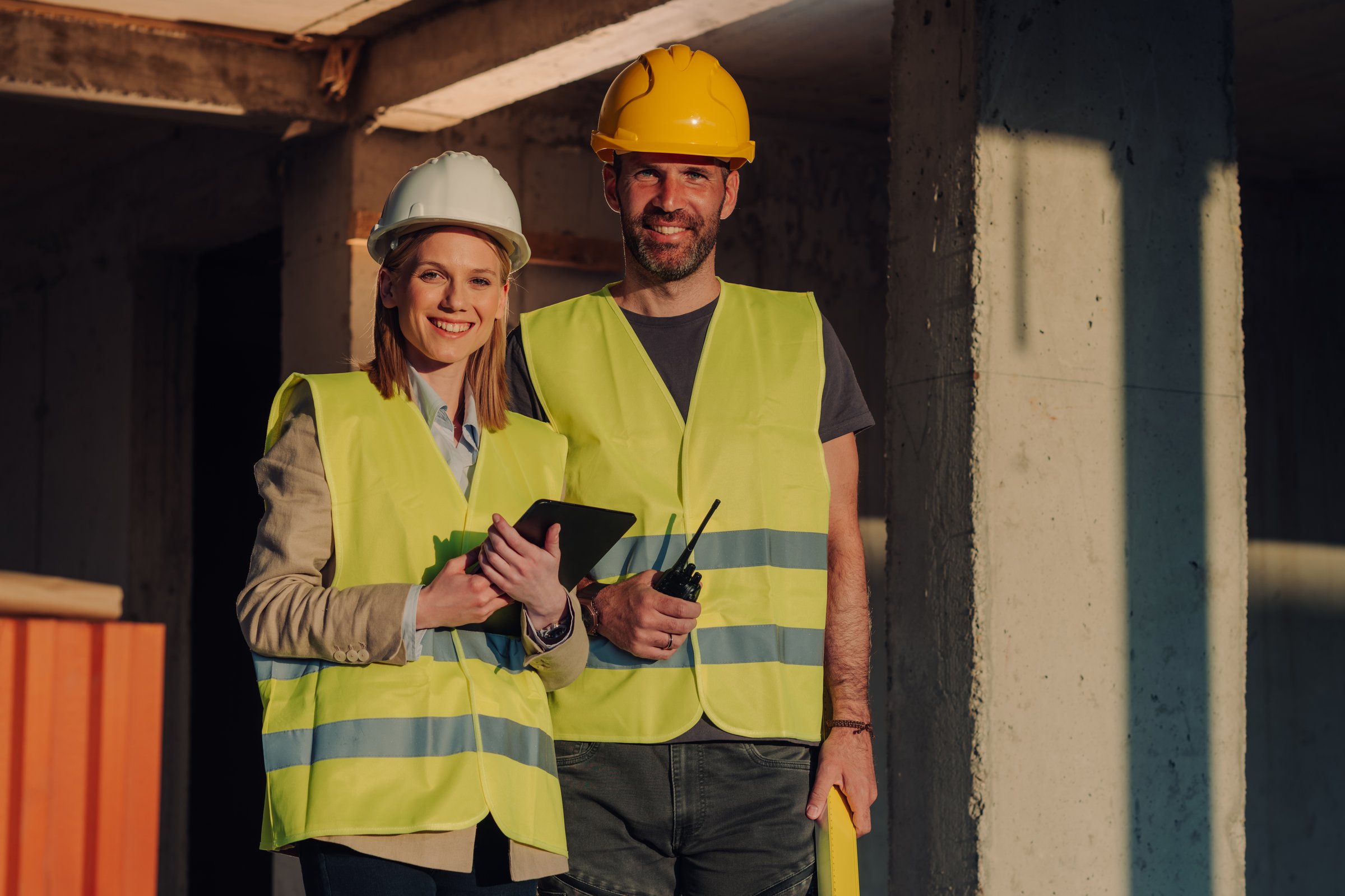 Construction workers are smiling and looking at the camera while holding a digital tablet and walkie-talkie