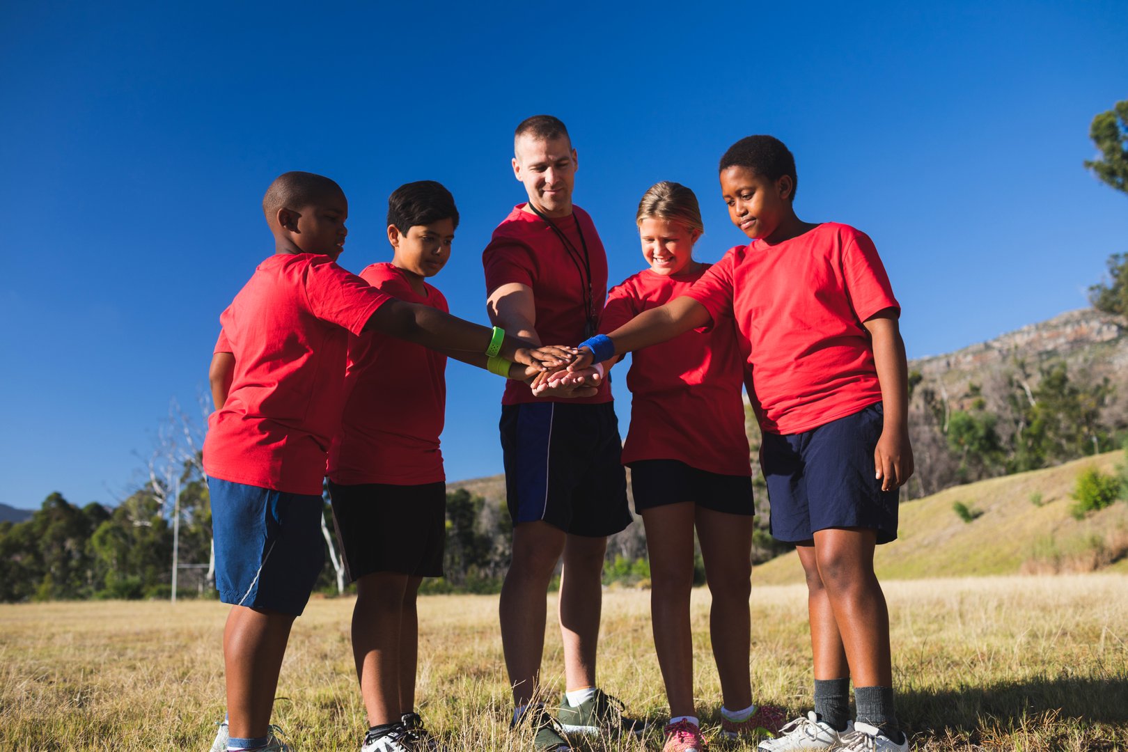 Trainer and kids forming hand stack in the boot camp on a sunny day