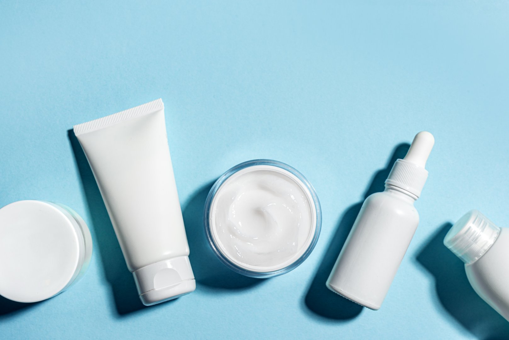 Various white cosmetic containers on blue background, creative layout, copy space. Blank facial beauty products, travel hygiene set, skin care minimal concept.