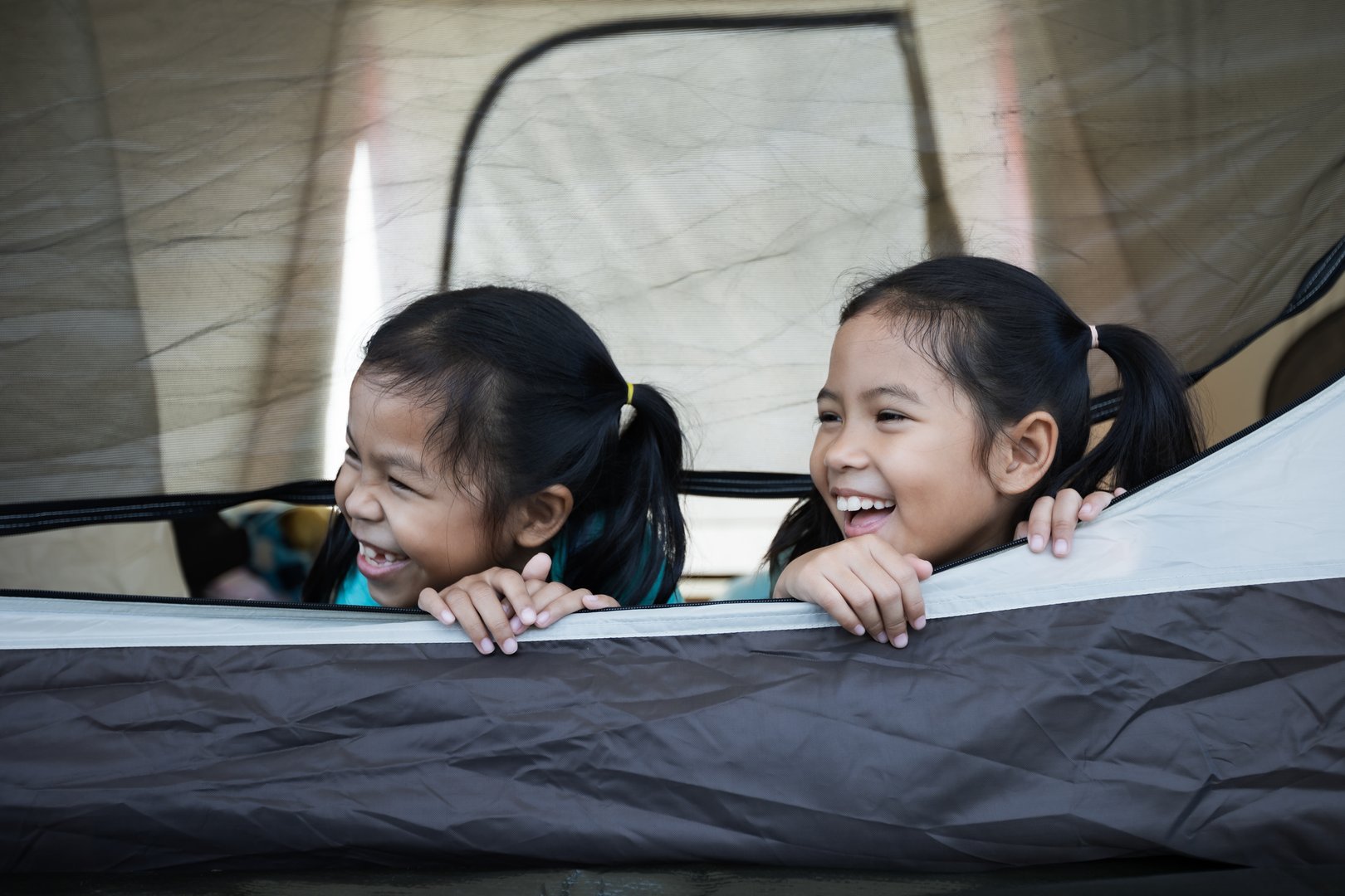 Two cute asian child girls lying down and playing together in tent on campsite while camping with family. Holiday and travel family camping concept.