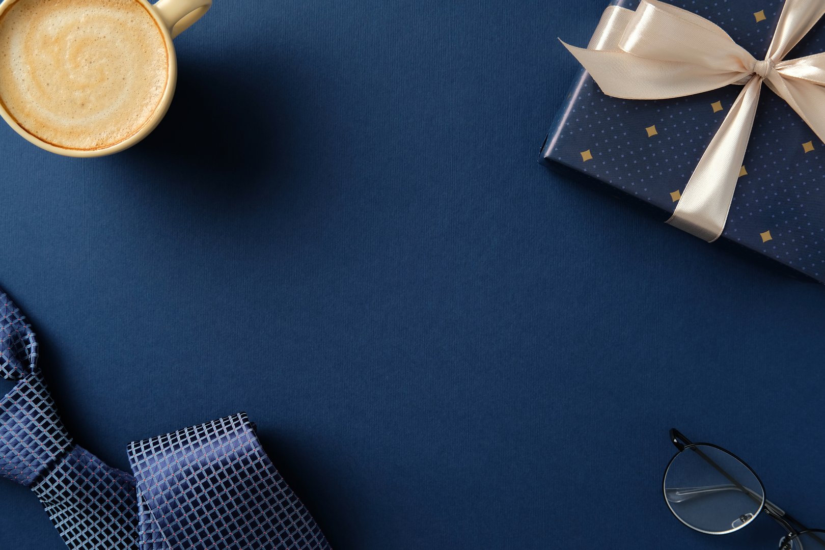 Happy Father's day concept. Flat lay composition with gift box, coffee cup, necktie and glasses on navy blue background.