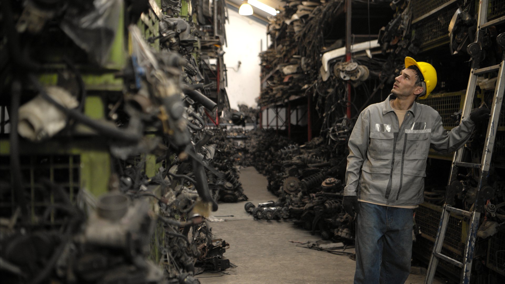 A factory worker wearing a safety helmet inspecting used car parts in an auto parts warehouse
