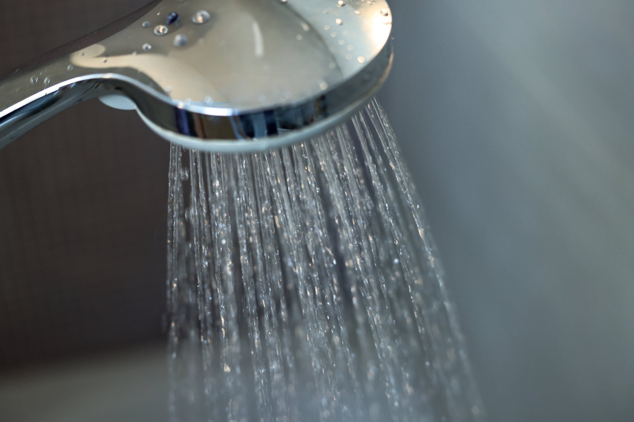 A sleek chrome shower head releasing a steady stream of water in a modern bathroom setting. The soft lighting and reflective surface enhance the sense of relaxation, hygiene, and self-care. Perfect for concepts of home wellness, spa, daily routine, and cleanliness.