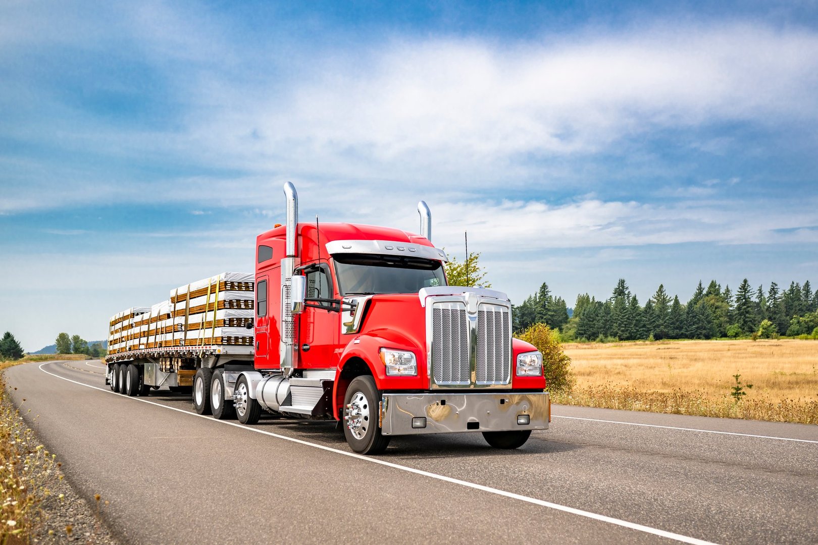 Industrial carrier red big rig semi truck tractor with extended cab for truck driver rest transporting fastened lumber cargo on flat bed semi trailer running on the summer road in Columbia Gorge area