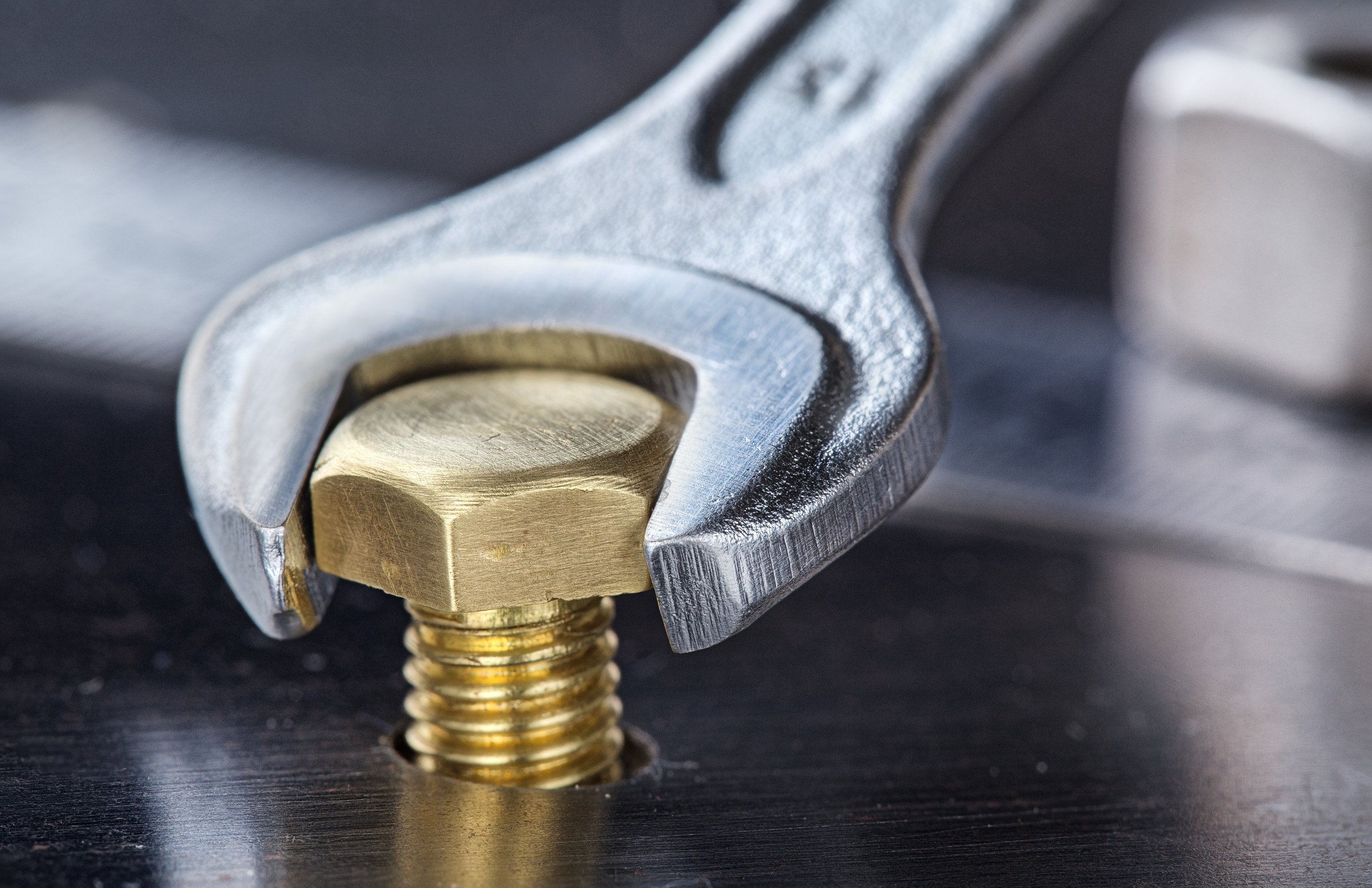 Wrench tightens bolt in steel billet. Spanner, bolt, screw and nuts.