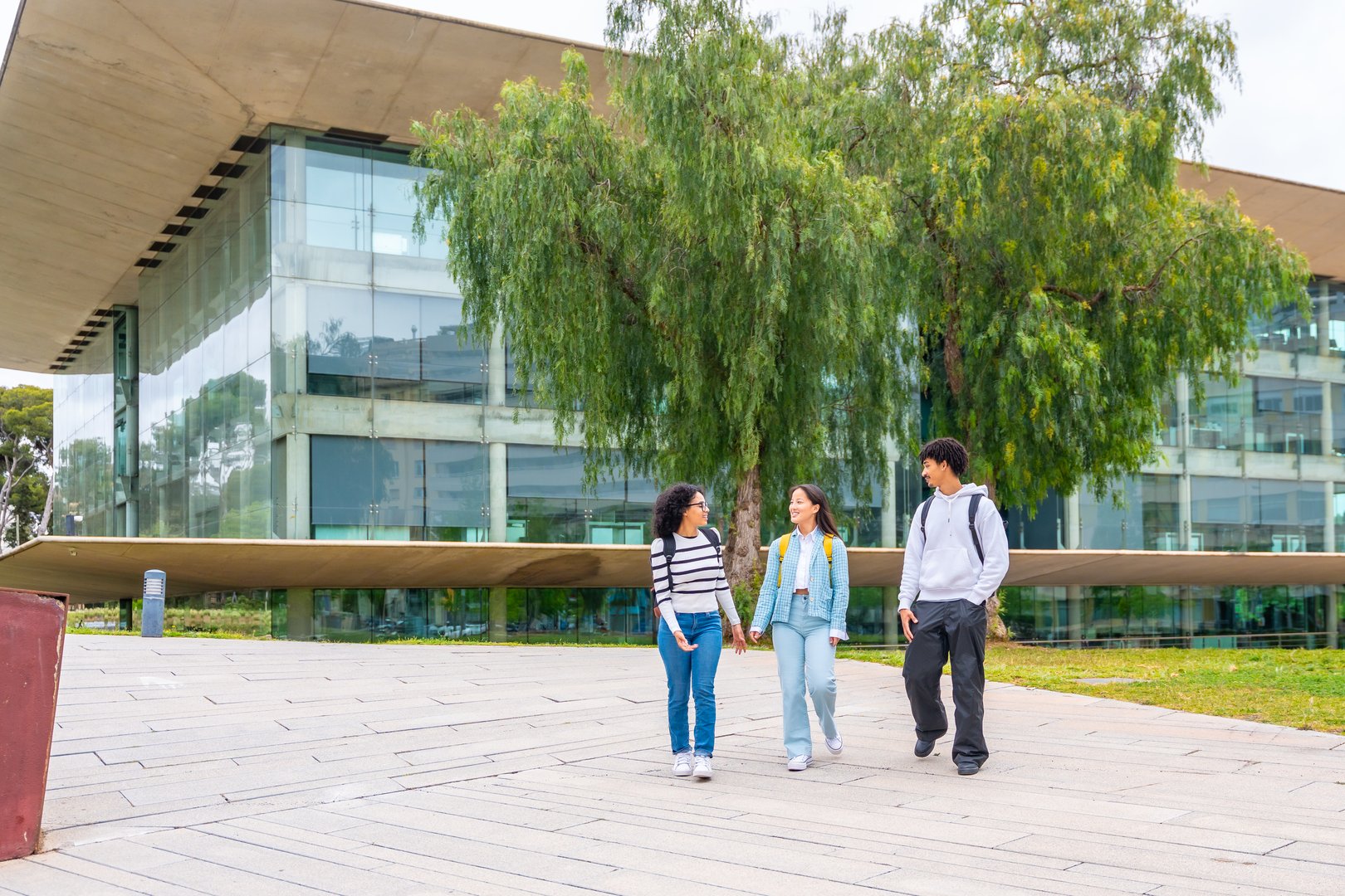 Three multi-ethnic students walking along the university campus