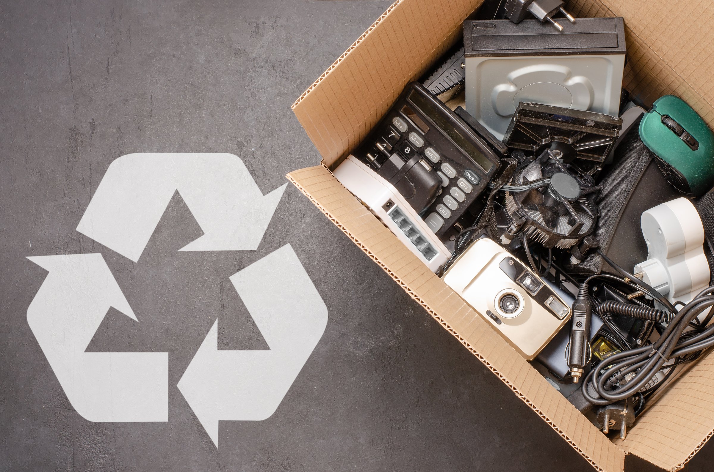 Old electronic devices in a cardboard box. The concept of recycling used gadgets. Black background.