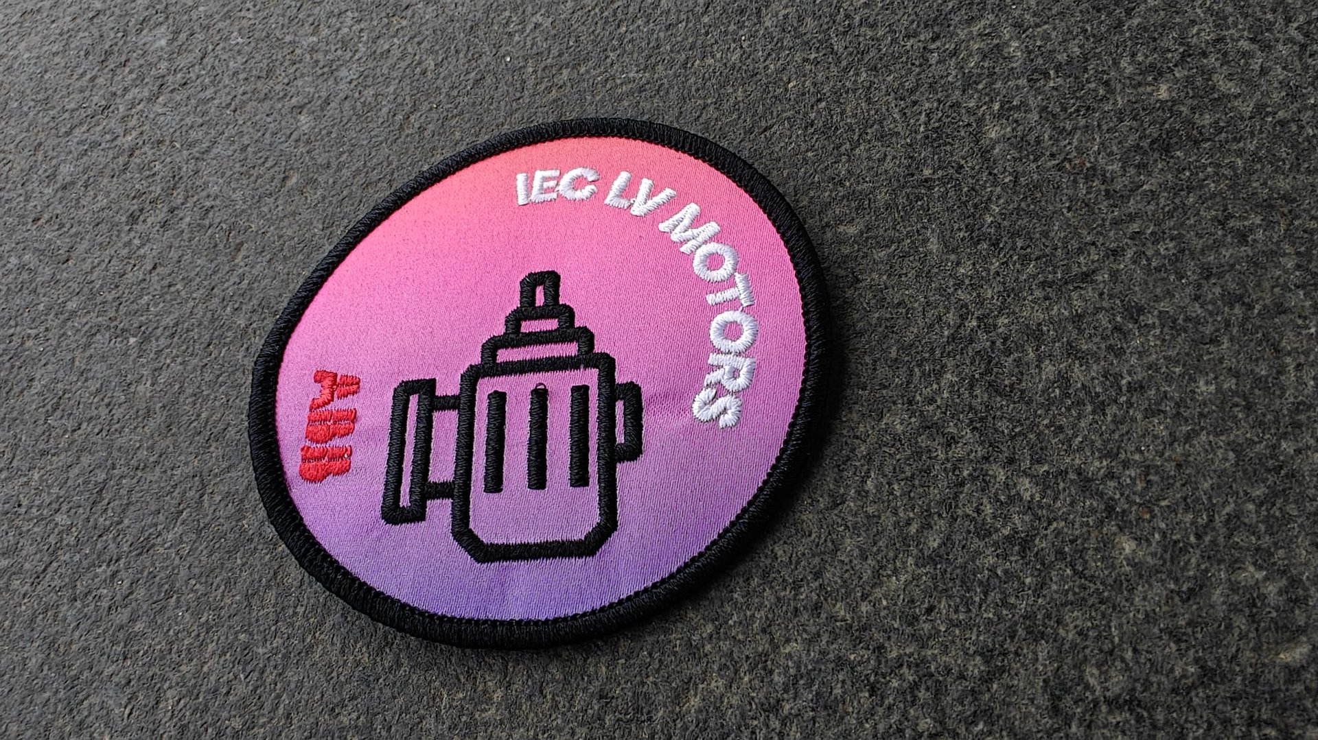A round patch with a gradient background featuring a motor illustration, text IEC LV MOTORS, and ABB logo on a textured surface.