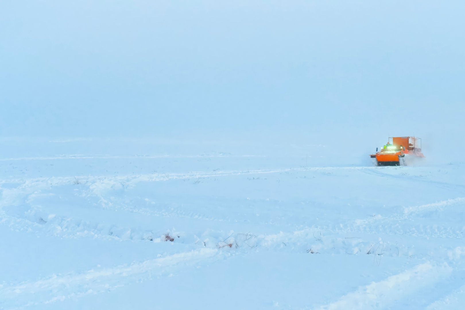Orange swamp vehicle on caterpillars driving through winter tundra, oil field