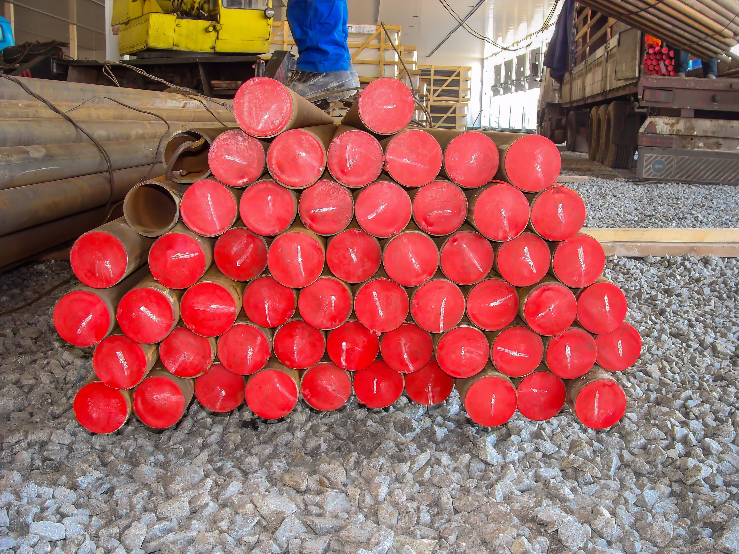 Close-up of steel pipes with red caps, neatly arranged on a construction site with gravel ground.