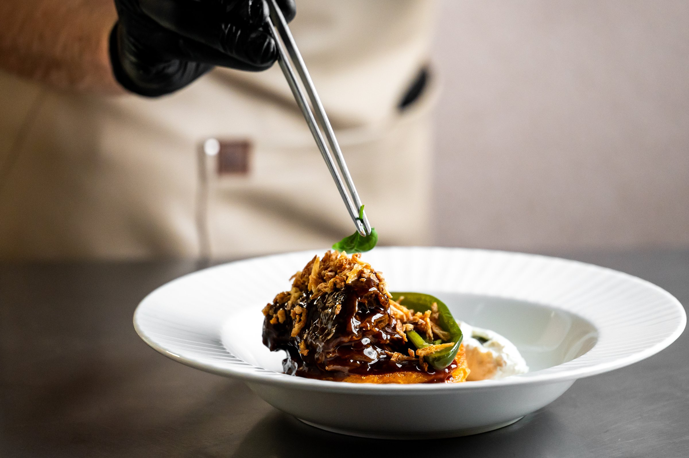 Chef carefully places a finishing garnish on a beautifully plated gourmet dish of braised beef cheeks. Fine dining, food styling, close-up, selective focus.